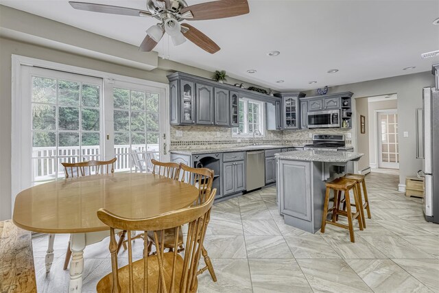 kitchen featuring gray cabinetry, appliances with stainless steel finishes, a ceiling fan, glass insert cabinets, and a sink