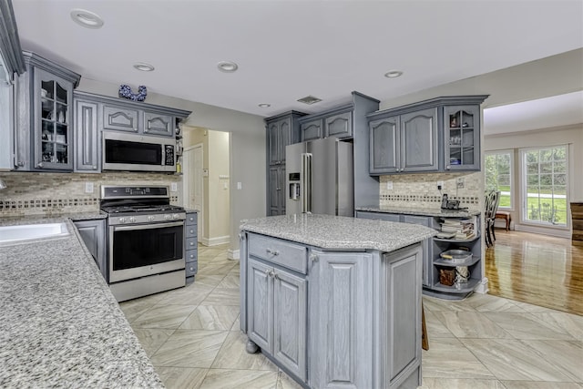 kitchen featuring appliances with stainless steel finishes, a sink, decorative backsplash, glass insert cabinets, and recessed lighting