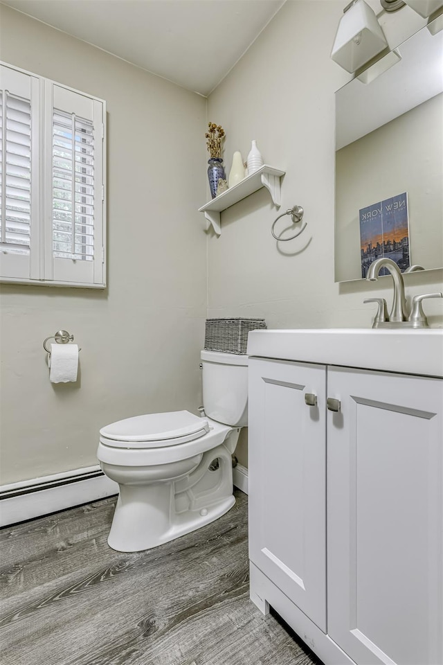bathroom featuring wood finished floors, baseboard heating, toilet, and vanity