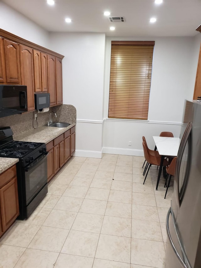 kitchen featuring black appliances, a sink, light stone counters, recessed lighting, and brown cabinetry