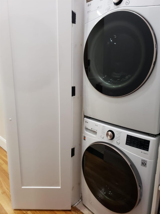 laundry area with stacked washer / drying machine and light wood-style flooring