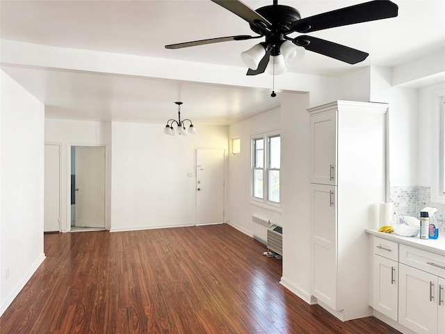 unfurnished dining area featuring dark wood finished floors, radiator, a chandelier, ceiling fan, and baseboards