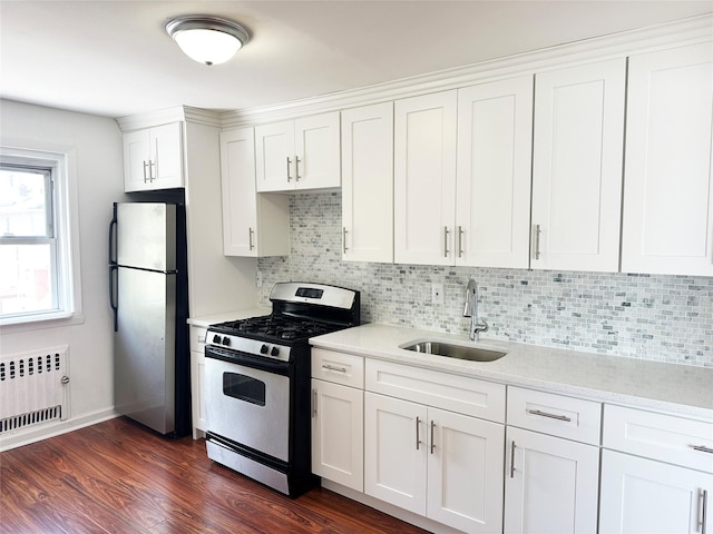 kitchen featuring appliances with stainless steel finishes, a sink, radiator, white cabinetry, and decorative backsplash