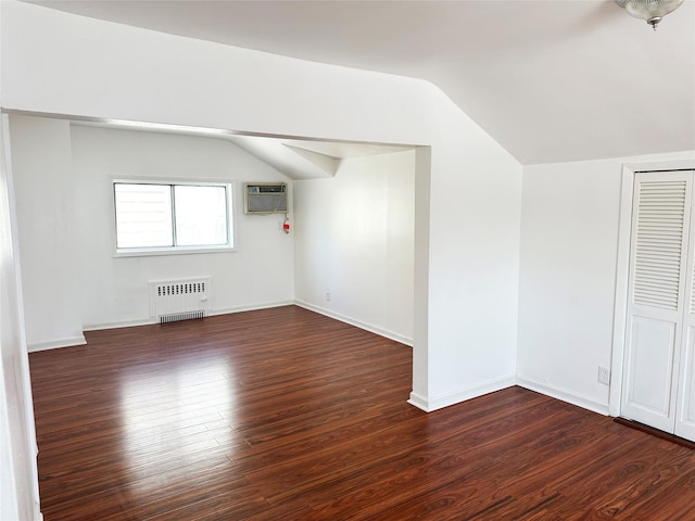 additional living space featuring radiator heating unit, a wall unit AC, dark wood-style floors, vaulted ceiling, and baseboards