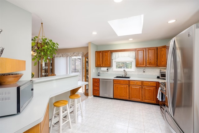 kitchen featuring appliances with stainless steel finishes, a sink, brown cabinets, a skylight, and decorative backsplash