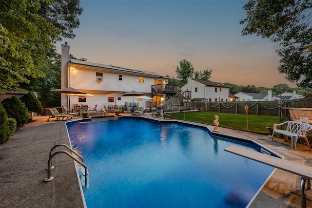 pool at dusk with a patio, stairs, a diving board, and a wooden deck