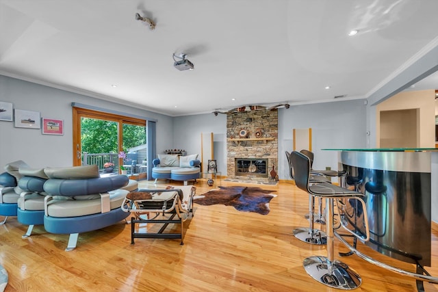 living area with wood finished floors, crown molding, a stone fireplace, a bar, and recessed lighting