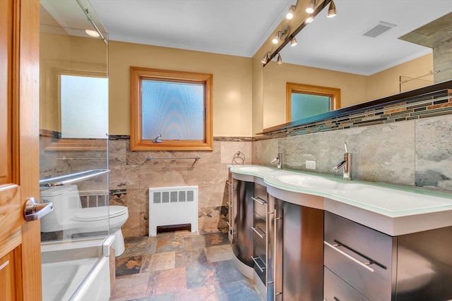 full bath with radiator heating unit, tile walls, toilet, vanity, and crown molding