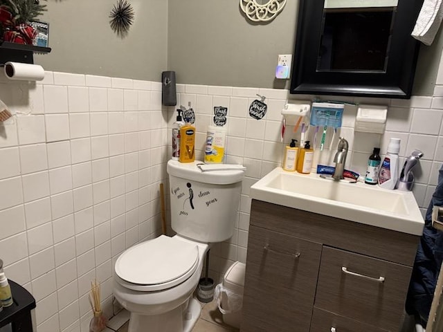 half bathroom with tile walls, toilet, vanity, wainscoting, and tile patterned flooring