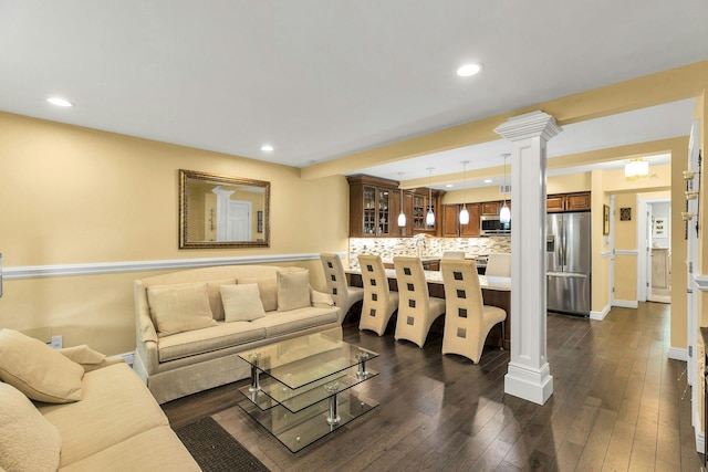 living room featuring dark wood-type flooring, decorative columns, baseboards, and recessed lighting