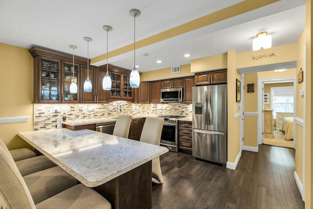 kitchen with appliances with stainless steel finishes, a peninsula, a kitchen bar, decorative backsplash, and recessed lighting
