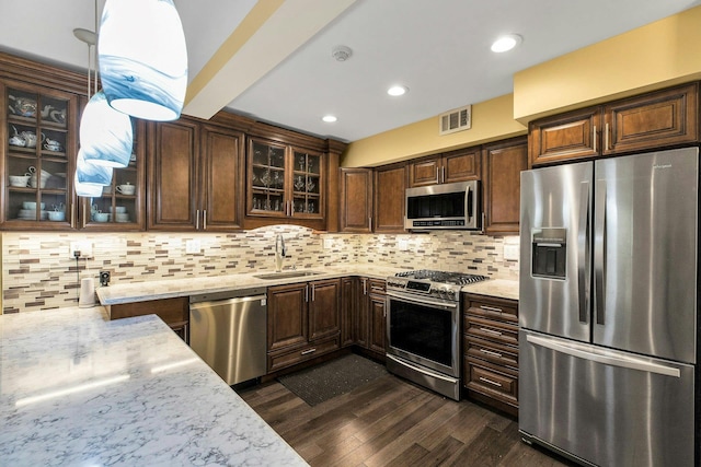 kitchen featuring stainless steel appliances, a sink, dark wood finished floors, light stone countertops, and dark brown cabinetry