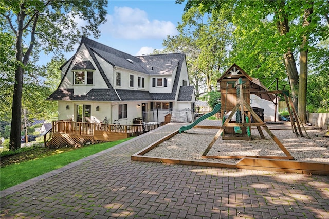 21 Judson Ave, Ardsley, NY 10502 - rear view of property featuring stucco siding, a playground, a wooden deck, and roof with shingles