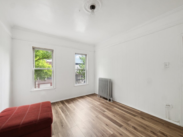 spare room featuring radiator, wood finished floors, ornamental molding, and baseboards