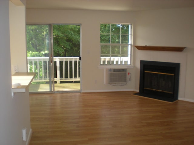unfurnished living room featuring wood finished floors, a fireplace with flush hearth, a wall mounted air conditioner, and baseboards