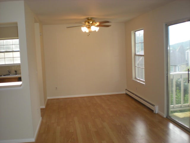 spare room featuring a baseboard radiator, light wood-style floors, ceiling fan, baseboards, and a sink