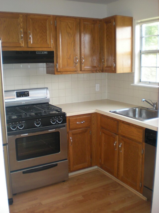 kitchen with stainless steel appliances, under cabinet range hood, a sink, brown cabinets, and light countertops