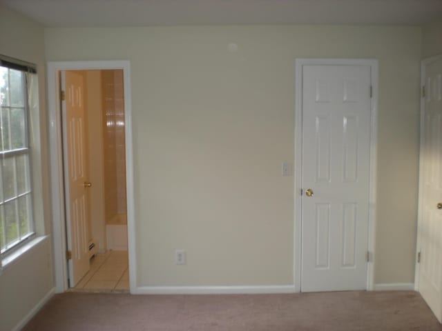 unfurnished bedroom featuring light colored carpet, baseboards, and ensuite bath