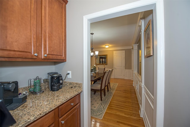 42 Kimberly Dr Unit 42, Westhampton, NY 11977 - kitchen featuring a decorative wall, light wood-style floors, crown molding, brown cabinets, and light stone counters