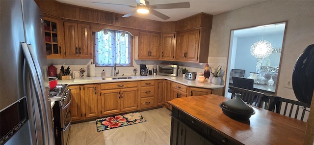 kitchen featuring stainless steel appliances, a sink, a chandelier, brown cabinets, and ceiling fan