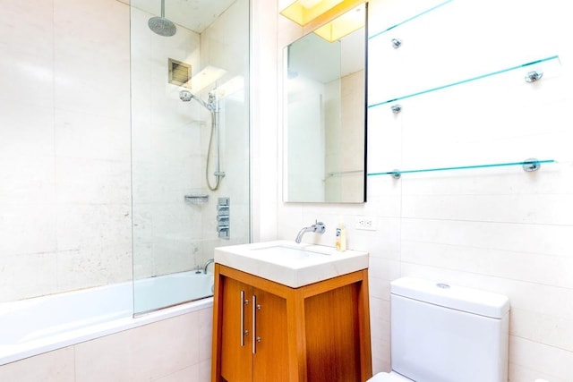 full bathroom featuring toilet, vanity, tiled shower / bath, and tile walls
