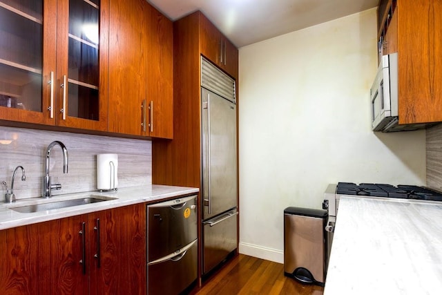 kitchen with a sink, appliances with stainless steel finishes, light countertops, decorative backsplash, and dark wood-style flooring