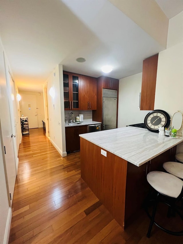 kitchen with built in fridge, a sink, light countertops, glass insert cabinets, and hardwood / wood-style flooring