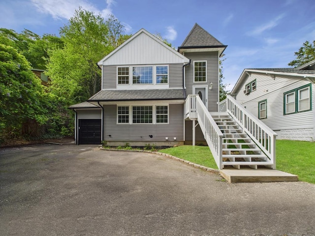 view of front of property with asphalt driveway, roof with shingles, board and batten siding, and a front yard