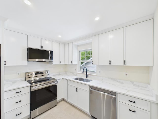 kitchen with appliances with stainless steel finishes, a sink, white cabinets, light stone countertops, and recessed lighting
