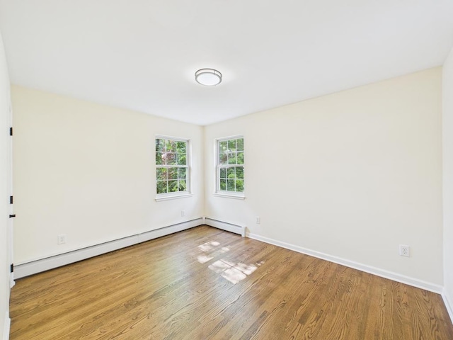 empty room with wood finished floors, a baseboard radiator, and baseboards