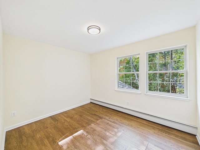 unfurnished room featuring a baseboard heating unit, wood finished floors, and baseboards