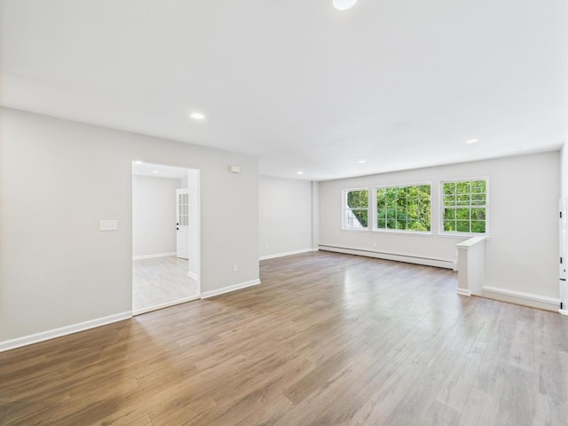 unfurnished living room with a baseboard heating unit, light wood finished floors, recessed lighting, and baseboards