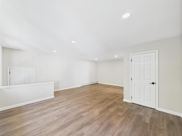 empty room with baseboard heating, wood finished floors, baseboards, and recessed lighting