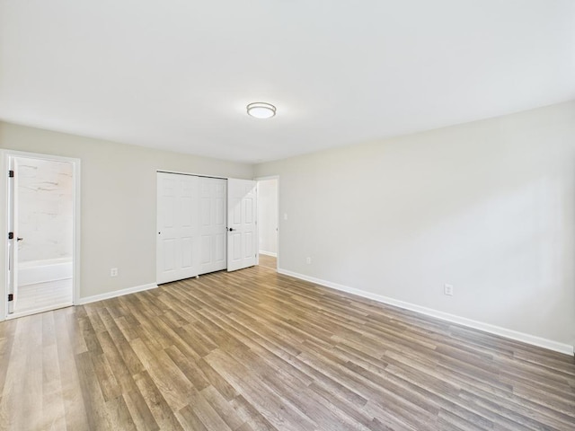 unfurnished bedroom with baseboards, light wood-style floors, a closet, and ensuite bath