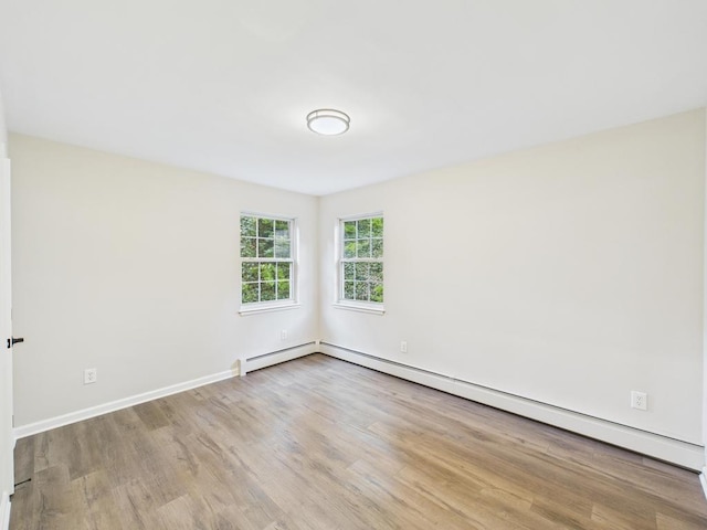 unfurnished room with baseboard heating, wood finished floors, and baseboards