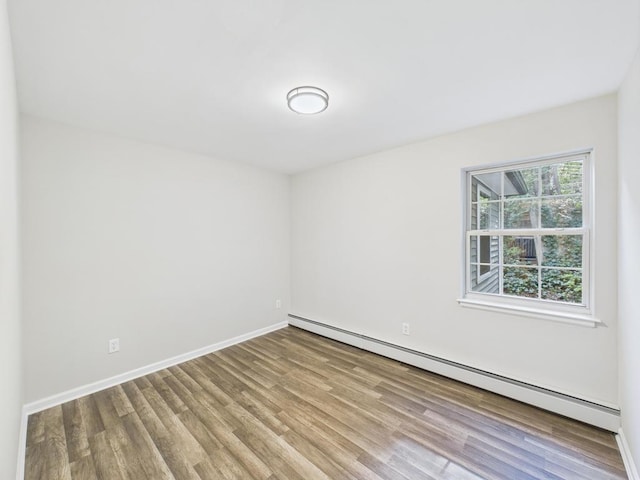spare room with a baseboard radiator, wood finished floors, and baseboards