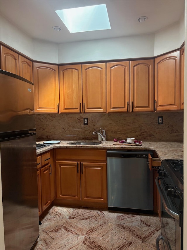 kitchen featuring dishwasher, gas range oven, freestanding refrigerator, a skylight, and a sink