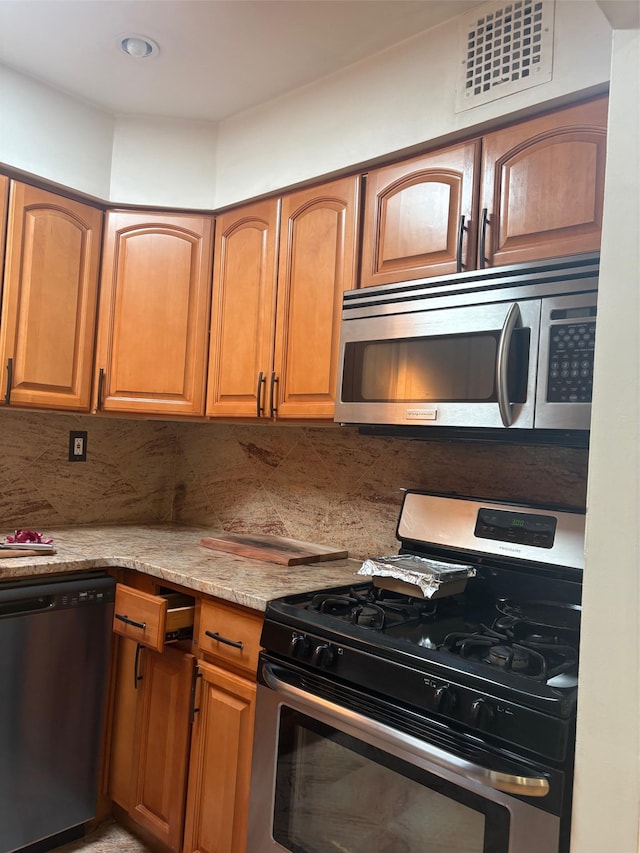 kitchen with stainless steel appliances, decorative backsplash, light stone countertops, and brown cabinetry