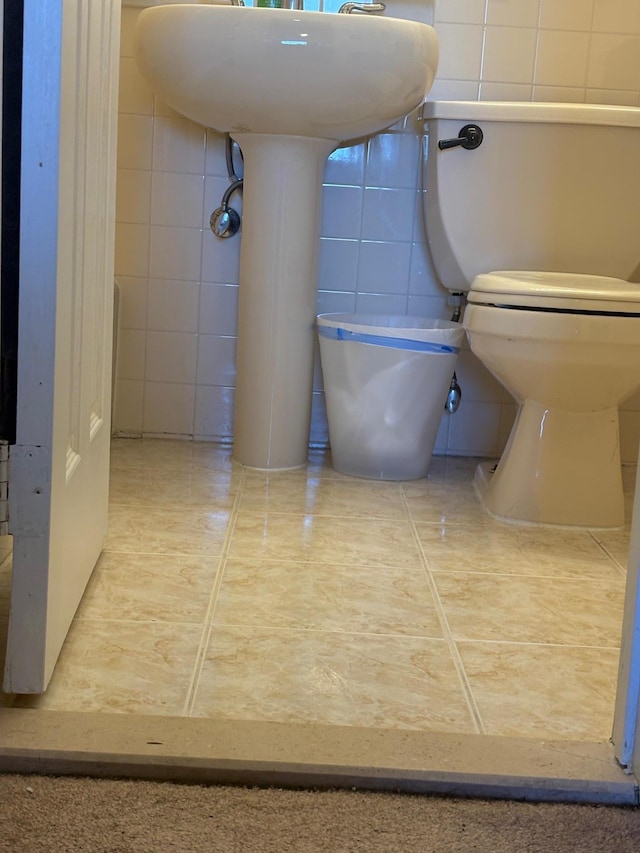 bathroom featuring tile walls, toilet, a sink, and tile patterned flooring