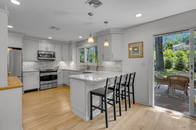 10 Bay Dr W, Huntington Bay, NY 11743 - kitchen featuring stainless steel appliances, a peninsula, a sink, backsplash, and light wood-type flooring