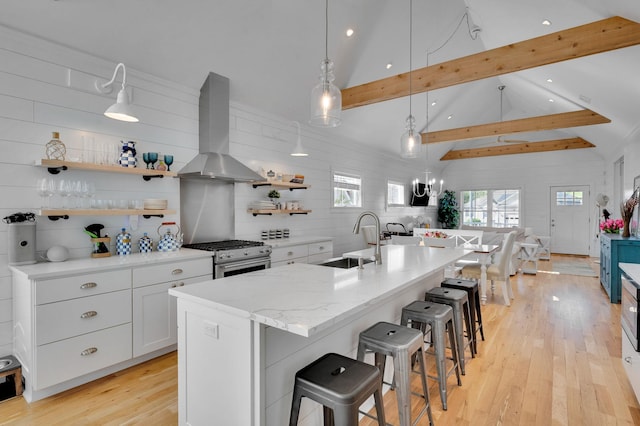 kitchen with a sink, wall chimney exhaust hood, stainless steel gas range oven, open shelves, and beam ceiling