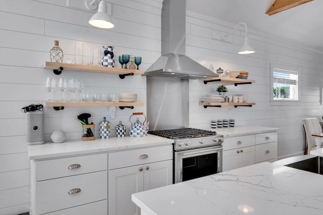 kitchen featuring stainless steel gas range oven, wall chimney range hood, open shelves, white cabinets, and light stone counters