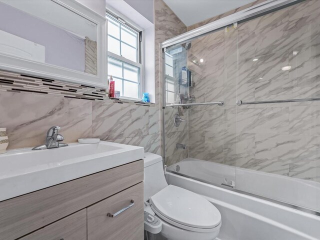 bathroom with toilet, bath / shower combo with glass door, vanity, and tile walls