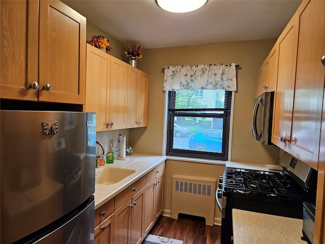 kitchen with stainless steel appliances, radiator, light countertops, a sink, and dark wood-style floors