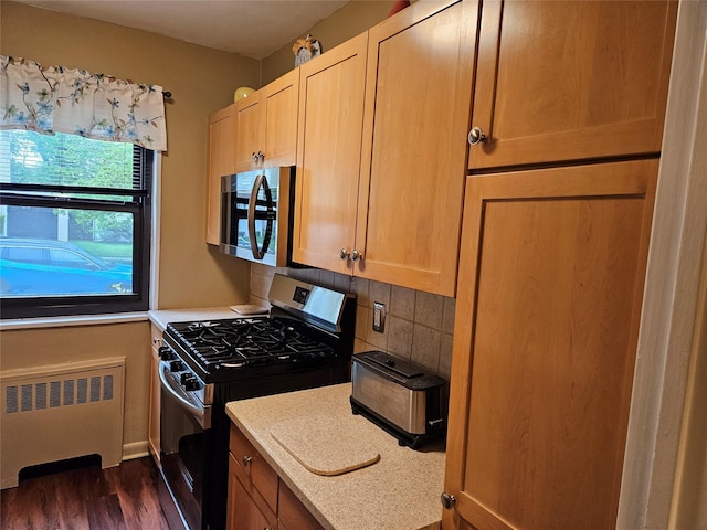 kitchen with stainless steel appliances, radiator, dark wood-style floors, light countertops, and backsplash