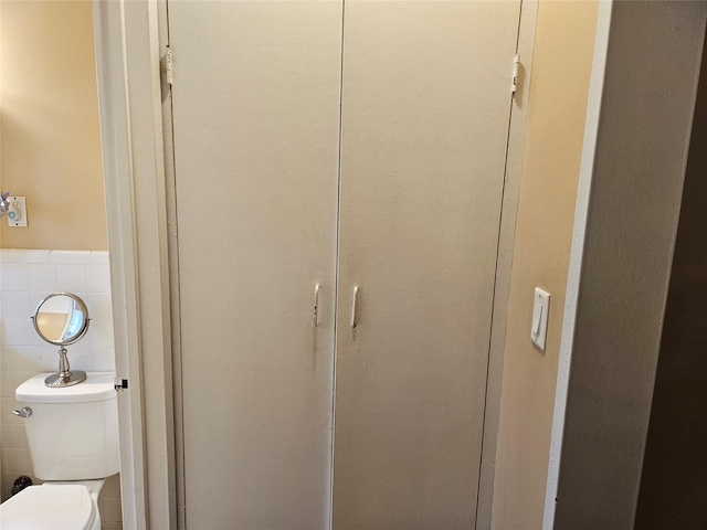 bathroom view of toilet, tile walls, and wainscoting