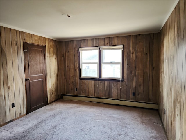 carpeted empty room featuring a baseboard heating unit and wooden walls