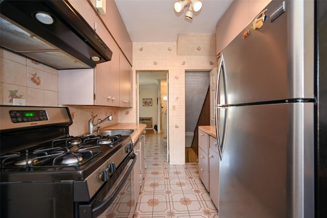 kitchen featuring stainless steel appliances, under cabinet range hood, a sink, light countertops, and tile walls