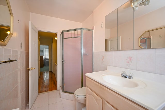 full bathroom featuring tile walls, a stall shower, tile patterned floors, toilet, and a wainscoted wall