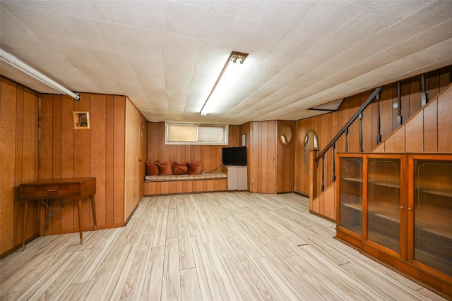 below grade area featuring stairs, light wood-type flooring, and wooden walls